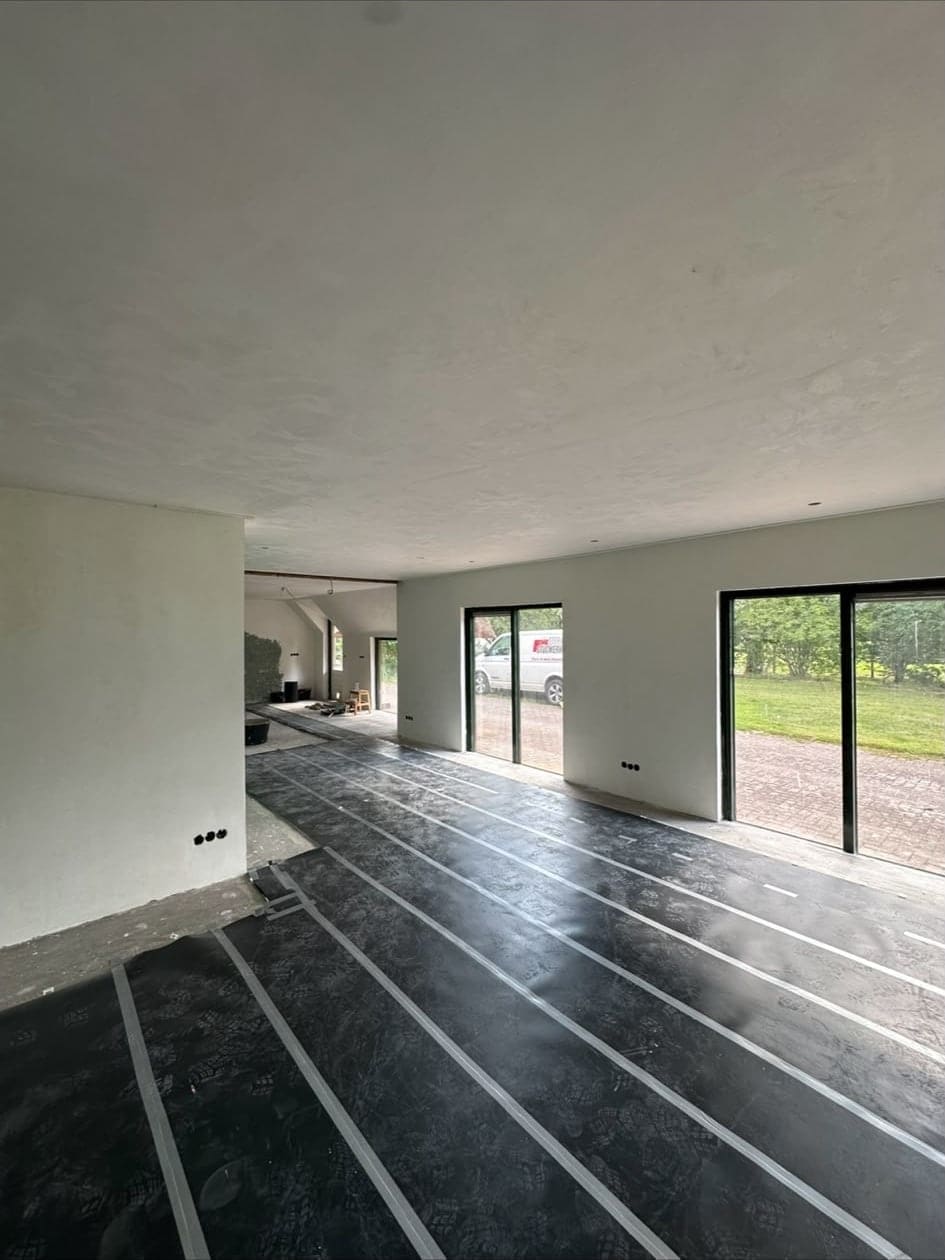 Ruime woonkamer met strak gestucte wanden en plafond en grote schuifpuien